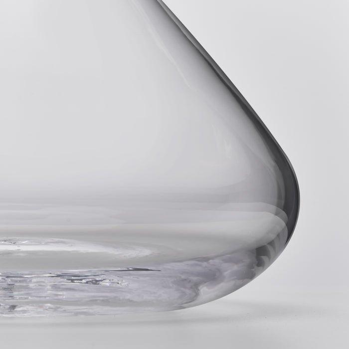 Clear glass wine decanter with curved spout and rounded body, shown at an angle against a white background.
