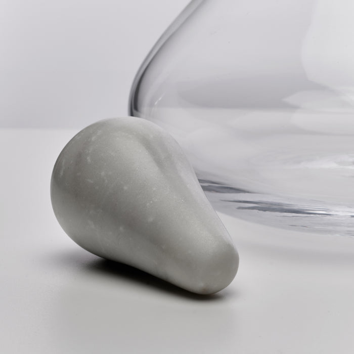 Teardrop-shaped marble stopper next to a clear glass decanter with curved body.