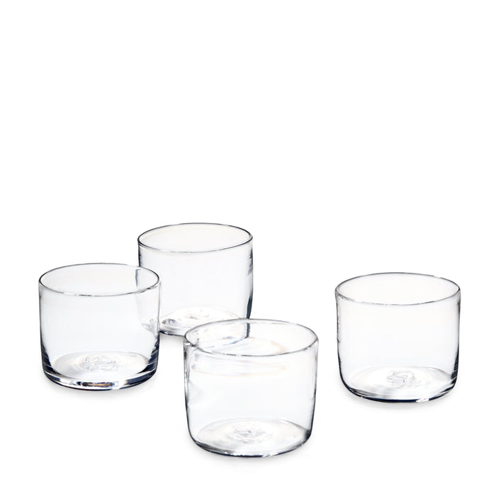 Four clear cylindrical drinking glasses with thick bases arranged in a group.