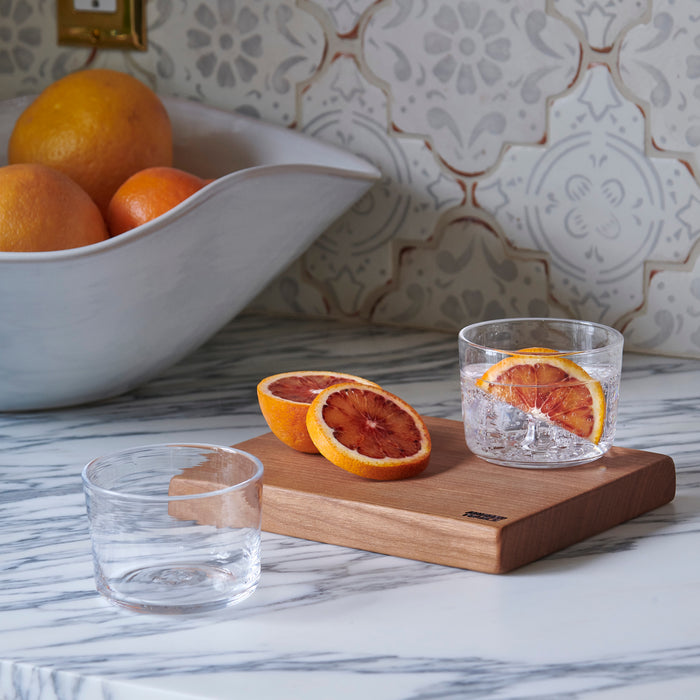 Four clear glass tumblers with grapefruit slices and ice, displayed on a wooden board.