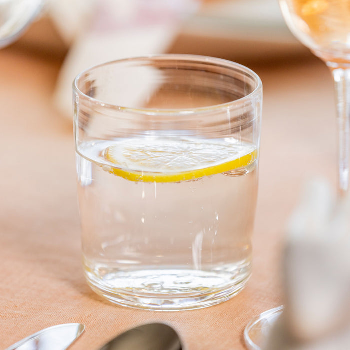 Clear glass tumbler filled with water and lemon slice, shown with additional glasses in background.