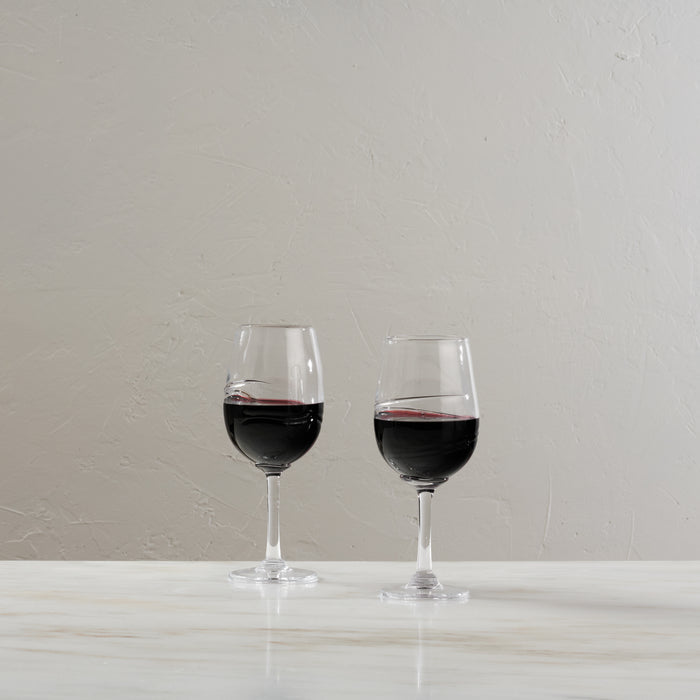 Two glasses filled with red wine on a white surface against a light gray textured wall.