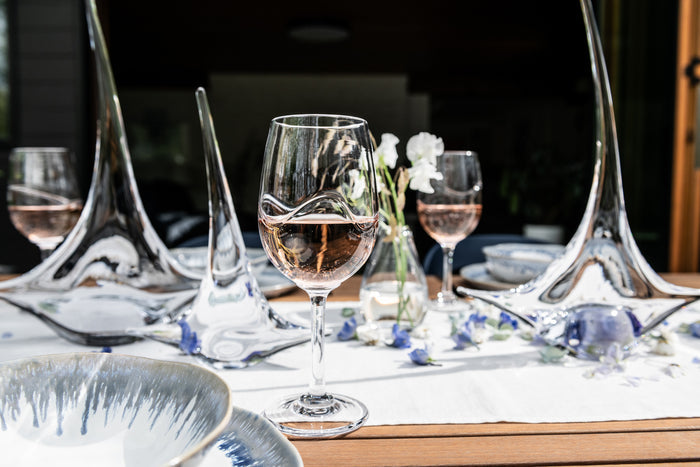 Wine glasses filled with red wine arranged on a formal dining table with place settings and white flowers.