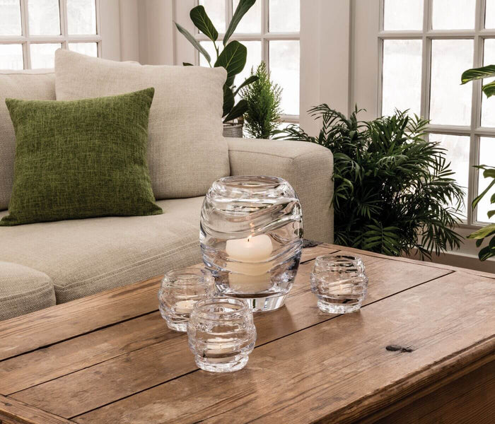 Clear glass tealight holders with white candles arranged on wooden table in living room setting.