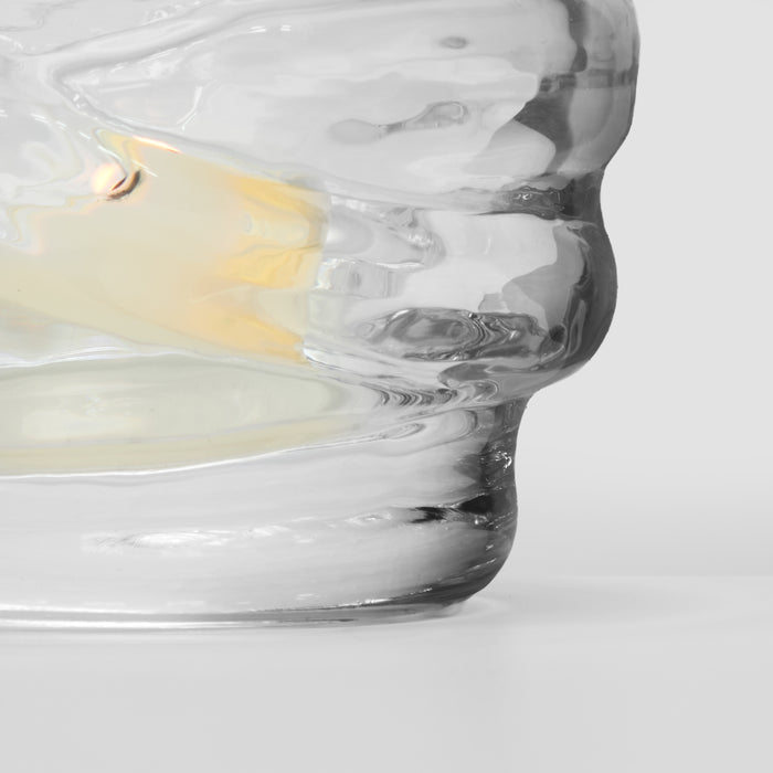Clear glass tealight holder with cream-colored candle and lit flame inside.