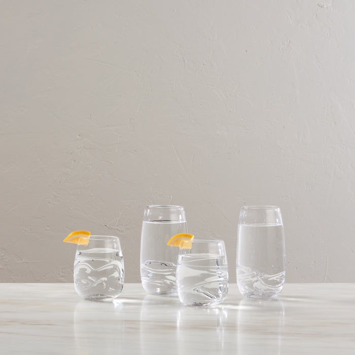 Four clear glass tumblers with swirl patterns, two garnished with orange slices, arranged on white surface.
