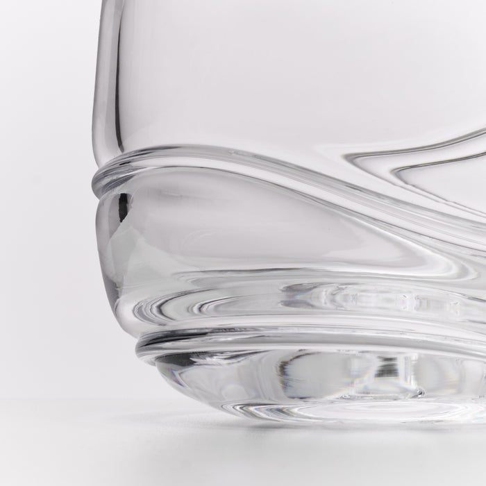 Close-up of a clear glass with a sculptural, wavy ribbed base on a white background.