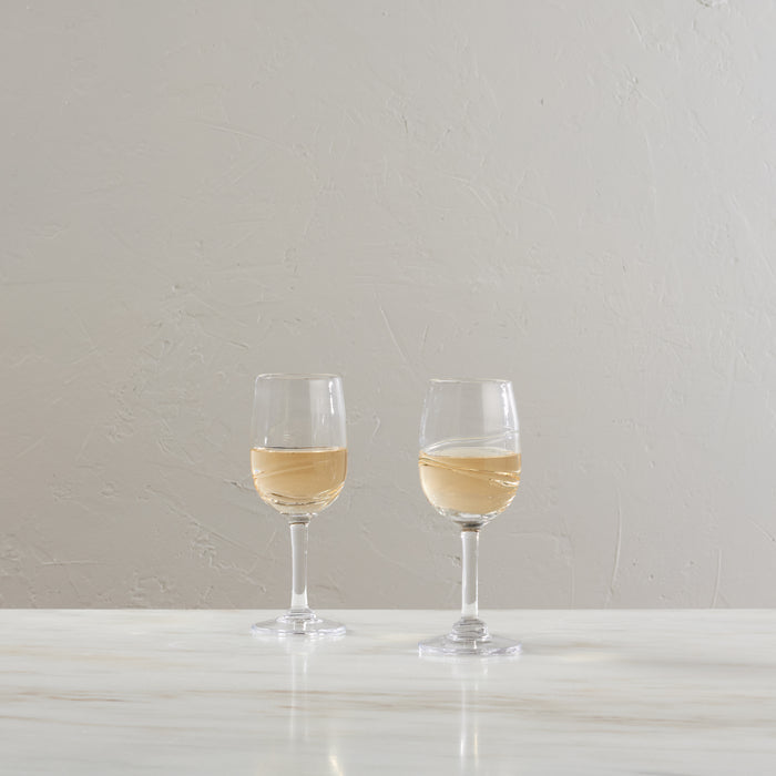 Two wine glasses filled with pale yellow white wine on a white surface against a textured gray wall.