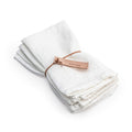 Four white linen napkins with hemmed edges, tied together with a copper-colored leather band.