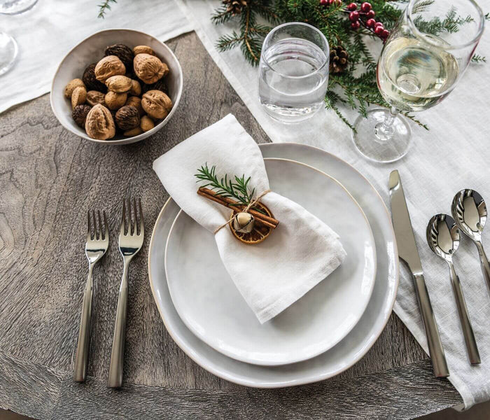 White linen napkin with hemstitched edge folded on place setting with holiday decoration.
