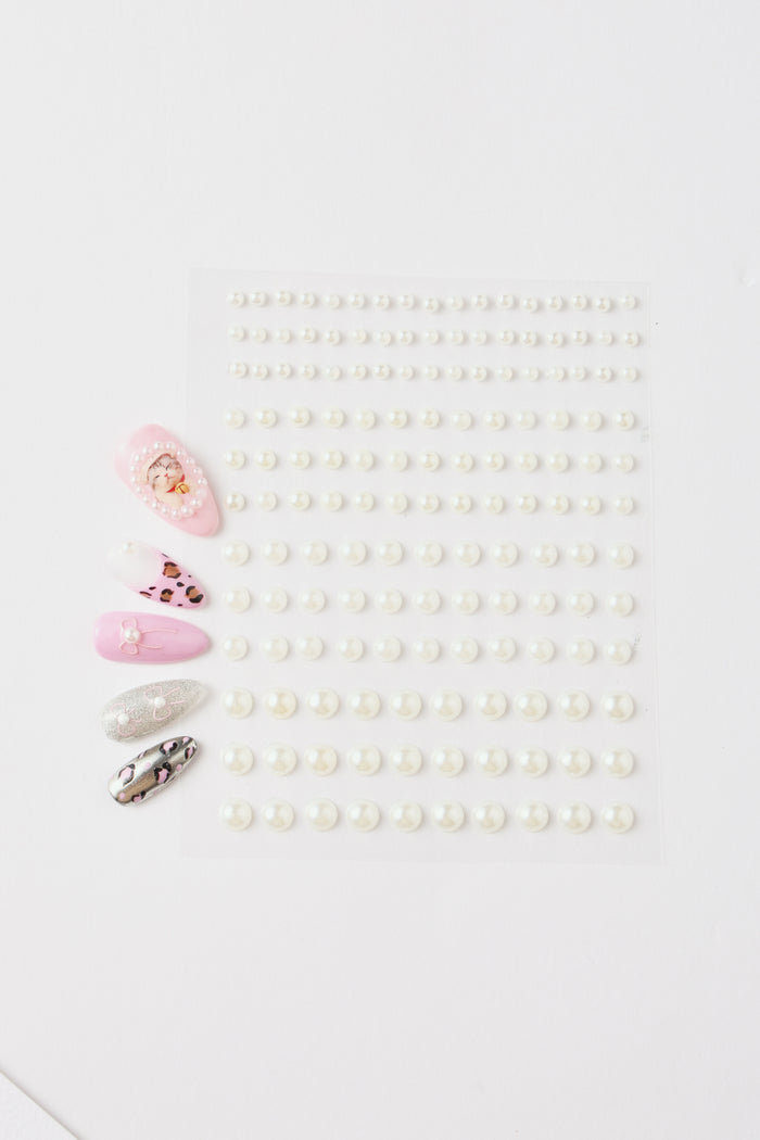 Sheet of white pearl nail stickers and four sample nails with pearl, leopard, and glitter designs.
