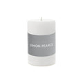White cylindrical pillar candle with gray band labeled "SIMON PEARCE" and visible wick on top.