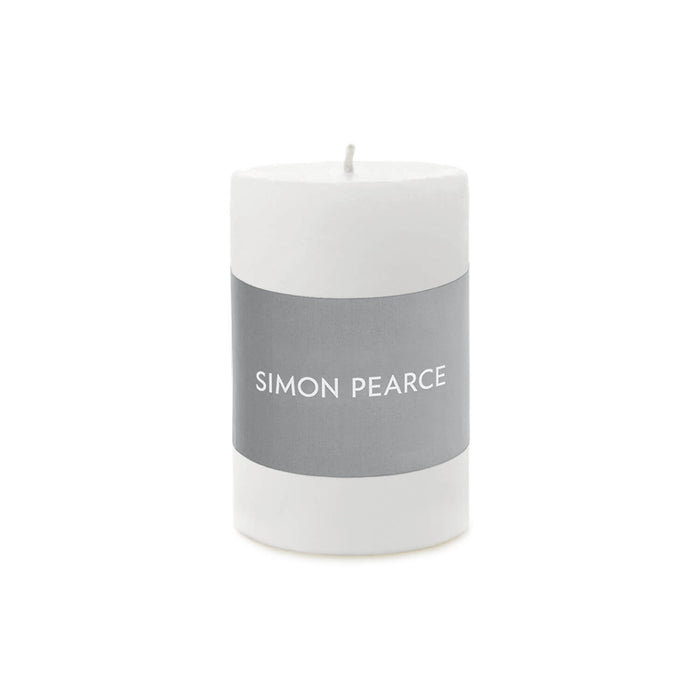 White cylindrical pillar candle with gray band labeled "SIMON PEARCE" and visible wick on top.