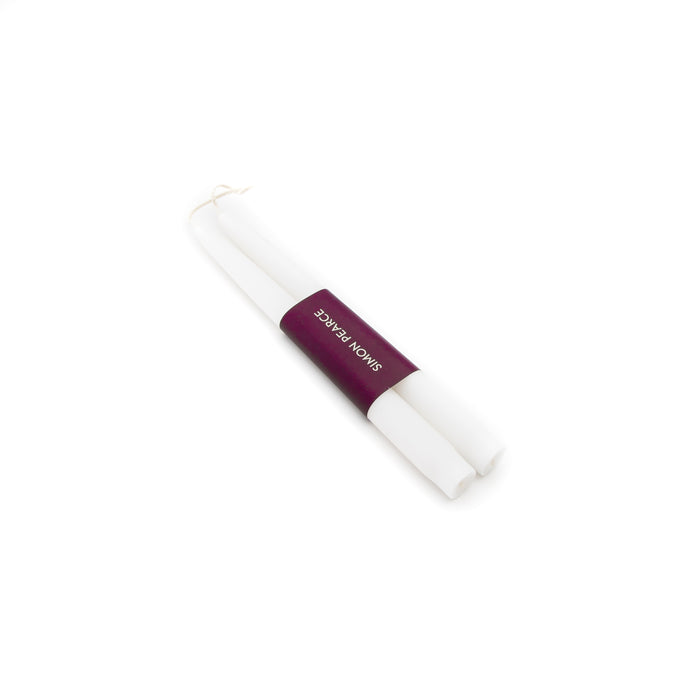Two white taper candles bundled together with a burgundy band labeled "DINEFORTWO'S".