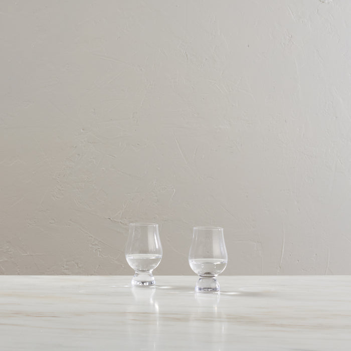 Two clear glass tasting glasses with footed bases displayed on a white surface.
