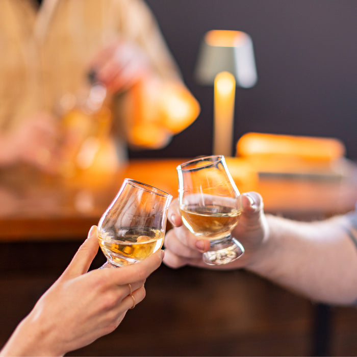 Two clear glasses filled with amber-colored liquor being held up in a toast.