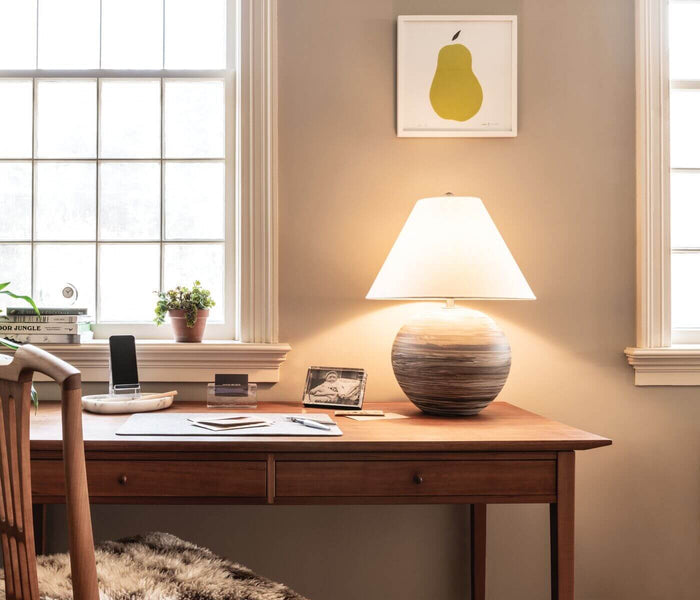 Brown leather cardholder displayed on wooden desk with lamp and decorative items.