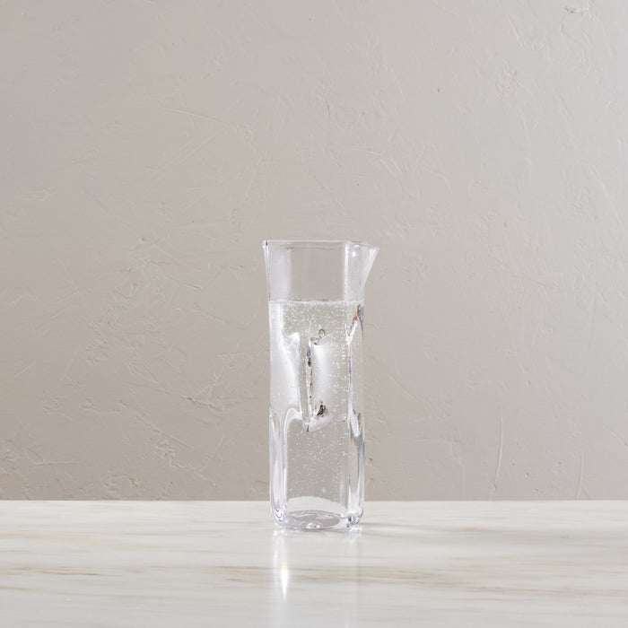 Clear glass carafe with tapered cylindrical shape, partially filled with carbonated water and ice cubes.