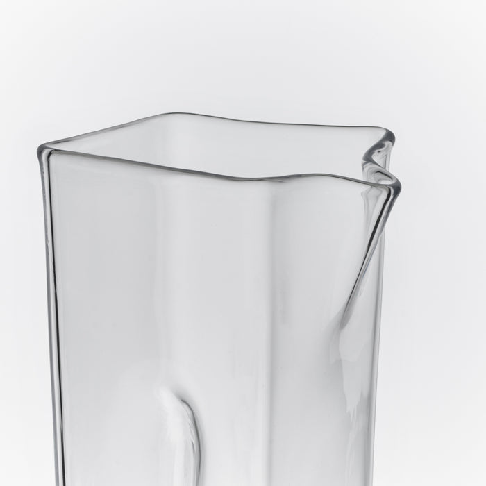 Clear glass carafe with curved wavy rim and pouring spout on one side.