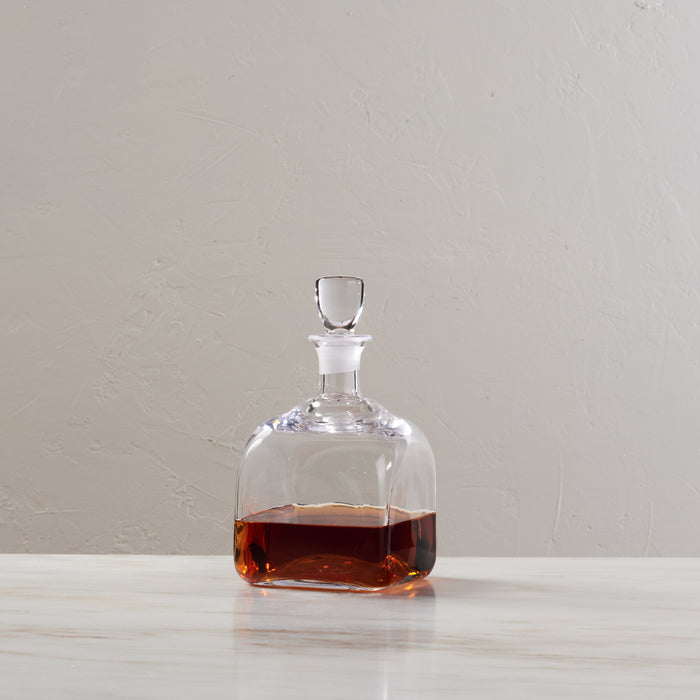 Clear glass decanter with stopper filled partially with amber liquid.