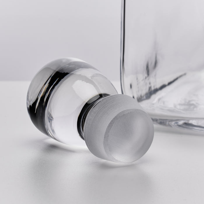 Clear glass decanter with a frosted stopper and black metal bands around the neck.
