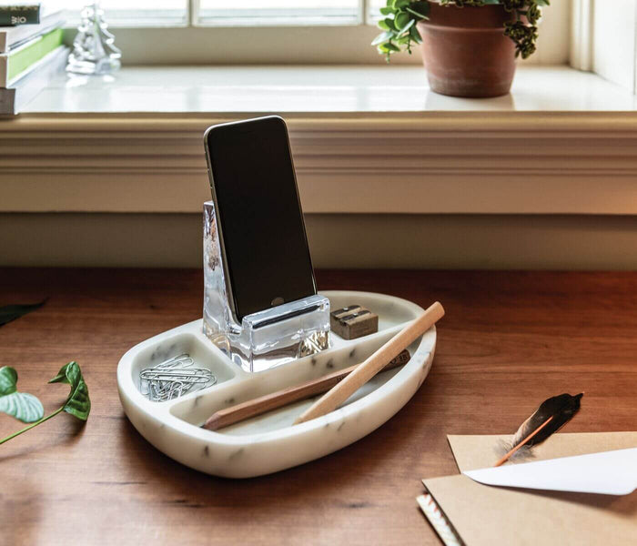 White marble desk caddy with phone stand, compartments holding paper clips, wooden pencils, and a small brush on a wooden des