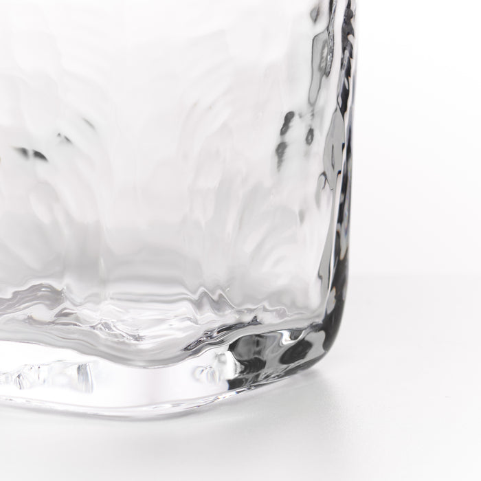 Close-up of a clear textured glass tumbler showing the corner and base detail against a white background.