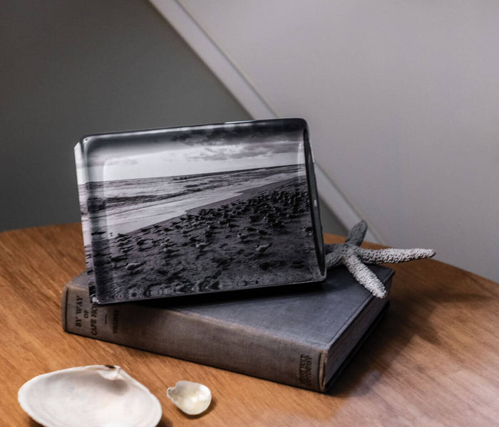 Horizontal acrylic photo block displaying black and white beach landscape scene, positioned on wood surface.