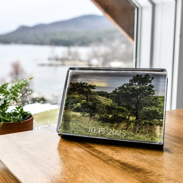 Clear acrylic photo block displaying landscape image with trees and date printed on surface, positioned on wooden table.