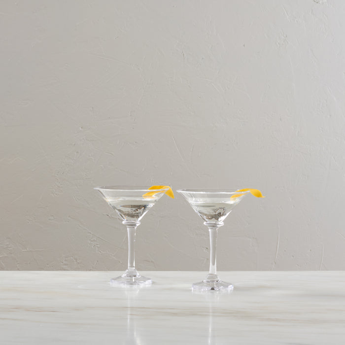 Two clear martini glasses filled with clear liquid and yellow lemon twists on rim.