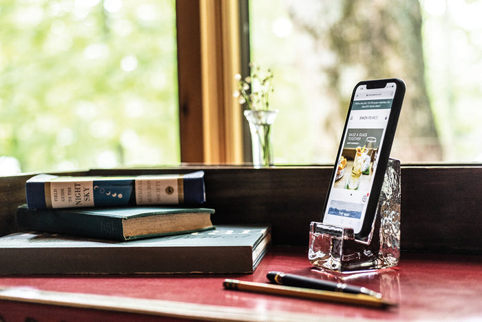 Clear acrylic phone holder displaying smartphone on desk with books and pen nearby.