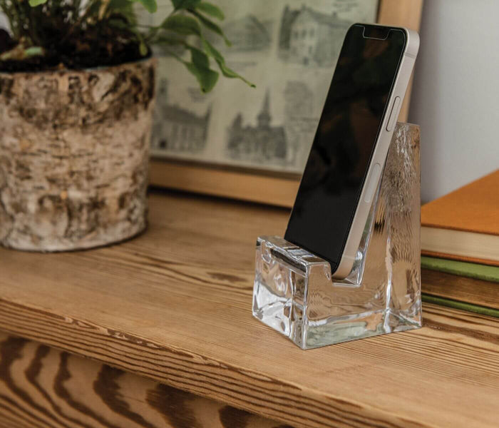 Clear acrylic phone holder with angled slot holding a smartphone upright on wooden desk.