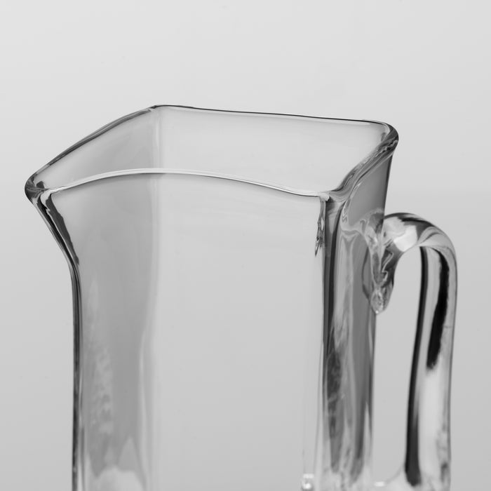 Clear glass pitcher with curved spout, flat sides, and handle on the right.