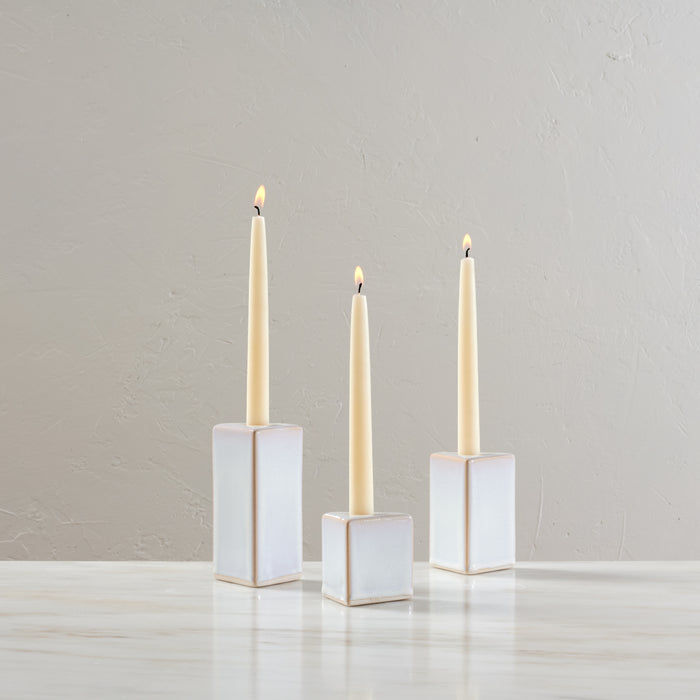 Three white ceramic taper holders with cream-colored lit candles in varying heights.