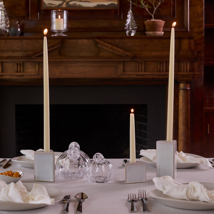 Cream-colored ceramic square taper candle holders holding lit tapered candles on a formal dining table.
