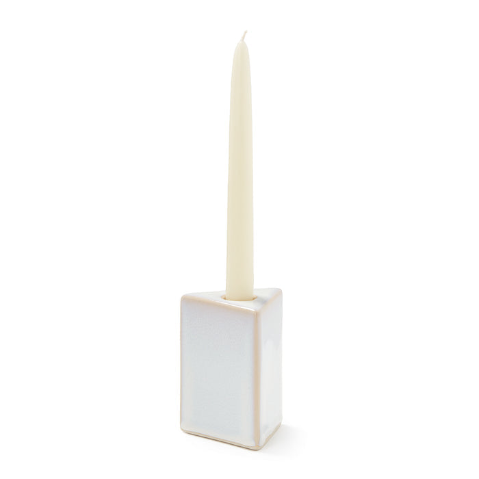 Cream-colored ceramic taper holder with square base holding a tall ivory taper candle.