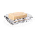 Clear glass soap dish with textured surface holding a cream-colored bar of soap.
