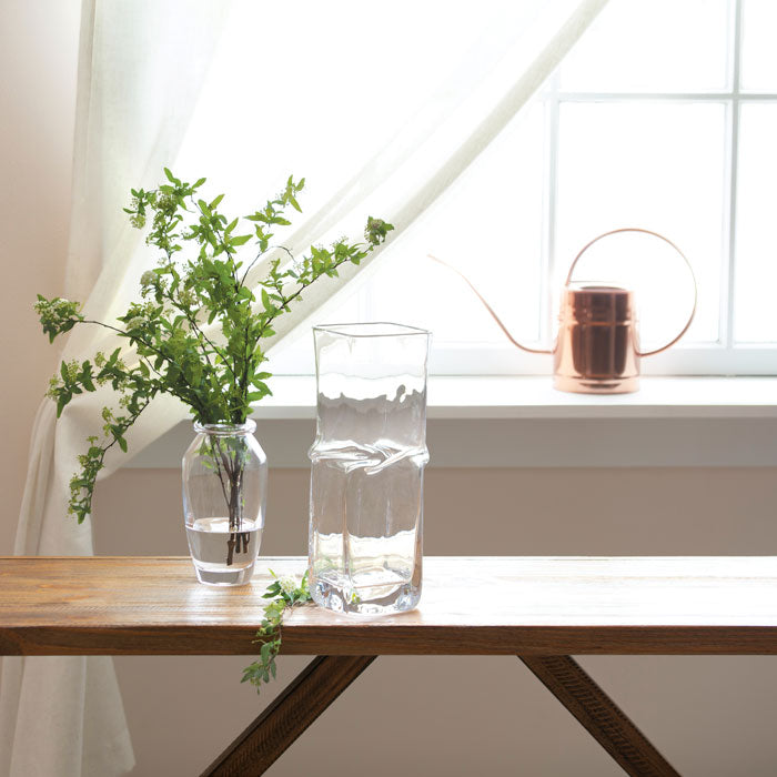 Clear glass vase with twisted cylindrical shape, filled partially with water, displayed on wooden table.