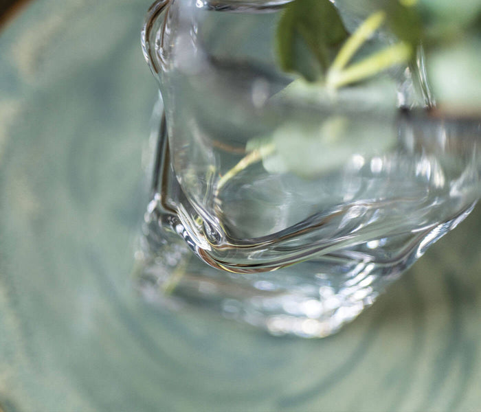 Clear glass vase with twisted texture detail holding green foliage stems.