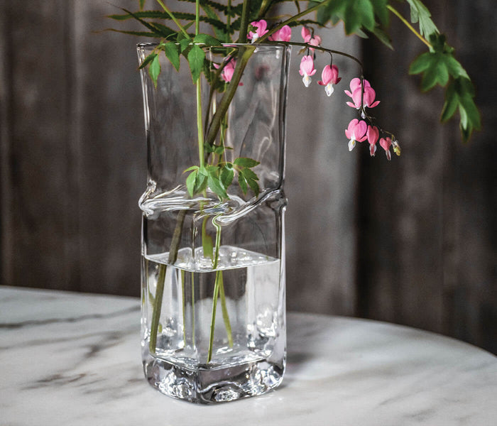 Clear glass vase with twisted center band containing pink flowers and green stems.