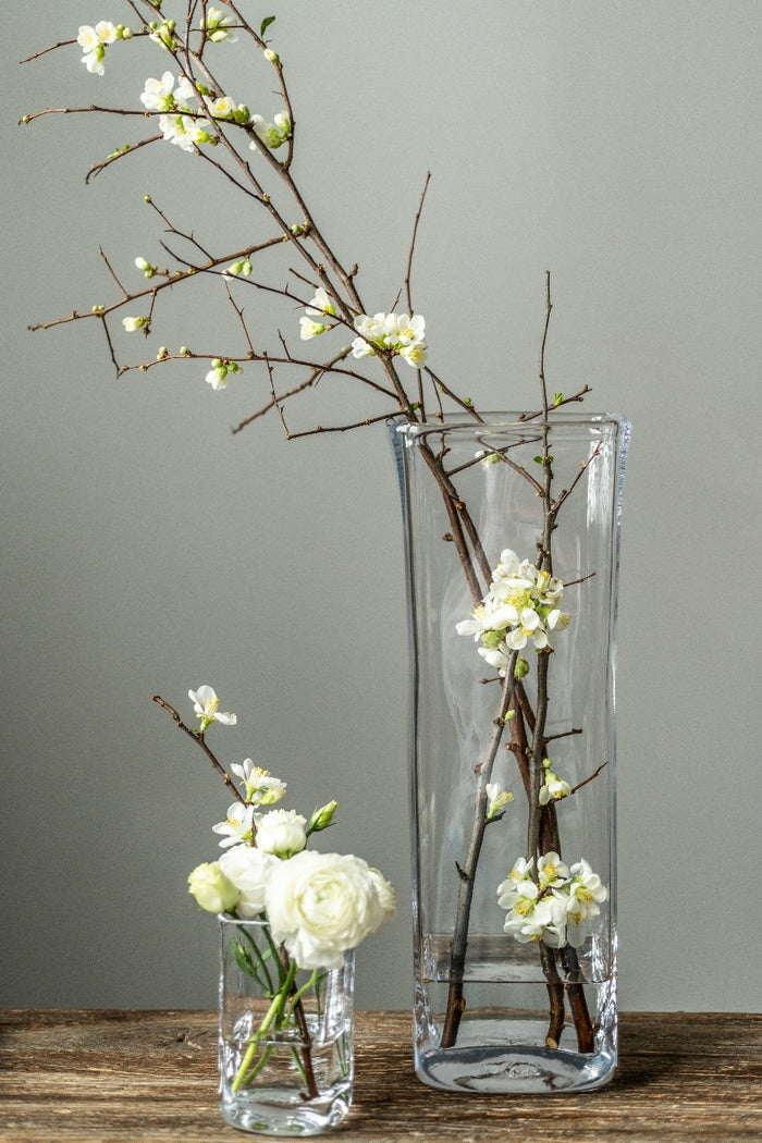 Clear glass rectangular vase with flowering branches and white blooms displayed inside.
