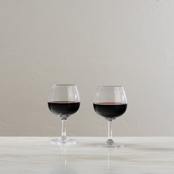Two balloon wine glasses filled with red wine on a white surface.