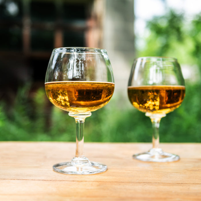 Two wine glasses filled with amber-colored wine on a wooden table with blurred outdoor background.