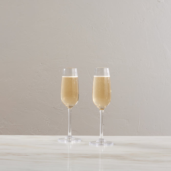 Two champagne flutes filled with sparkling wine on a white surface against a neutral background.