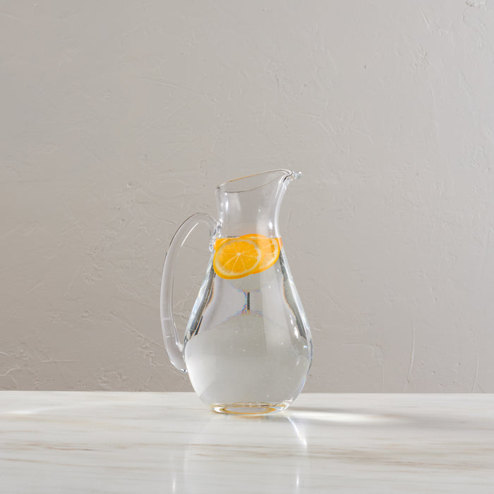 Clear glass pitcher with handle containing water and an orange slice.