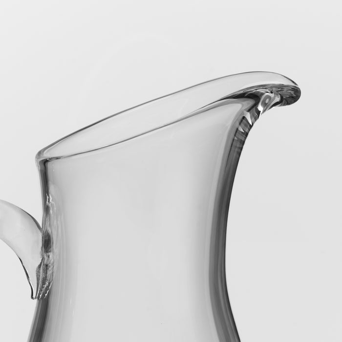 Clear glass pitcher with curved body and flared rim spout.
