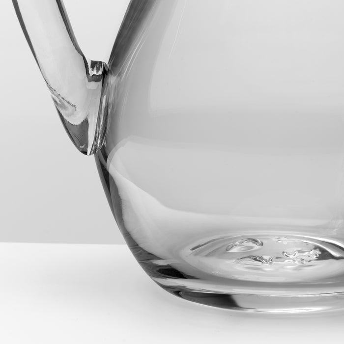Large clear glass pitcher with curved handle and wide spout, shown against white background.