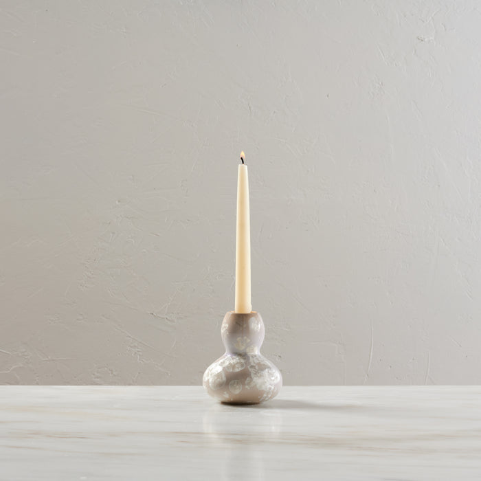 Cream-colored pottery candlestick with bulbous base holding a lit cream taper candle.