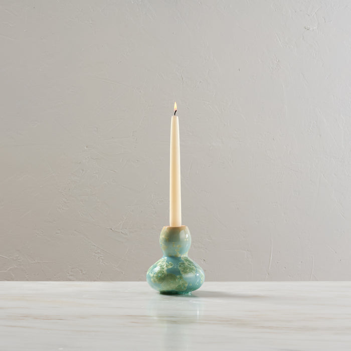 Ceramic candlestick with green and blue glazed bulbous base holding a lit taper candle.