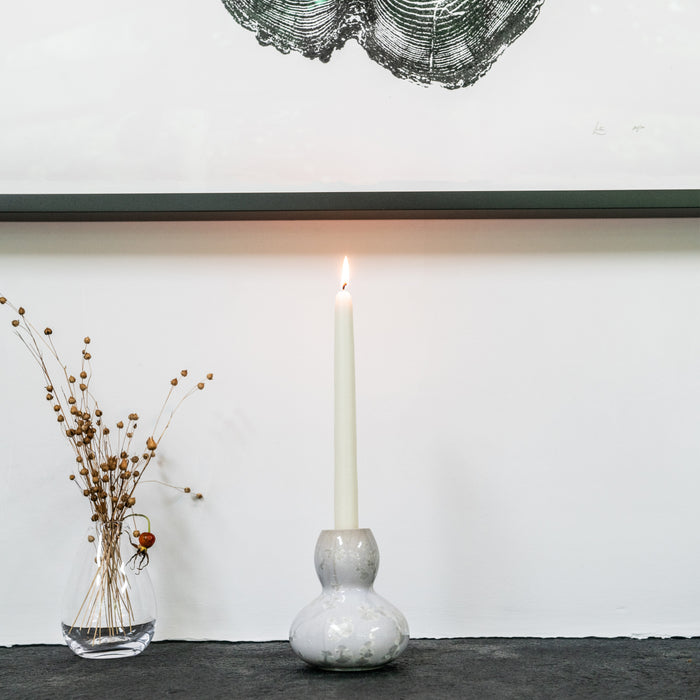 White ceramic candlestick with bulbous base holding a lit cream taper candle.